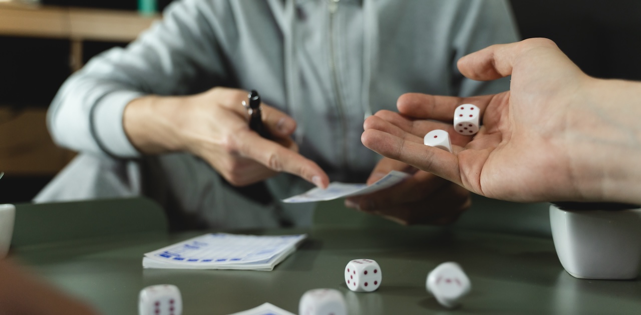 Two players playing bunco. One player has a pair of dice in their hand. The other player is pointing to a scorecard in their other hand.