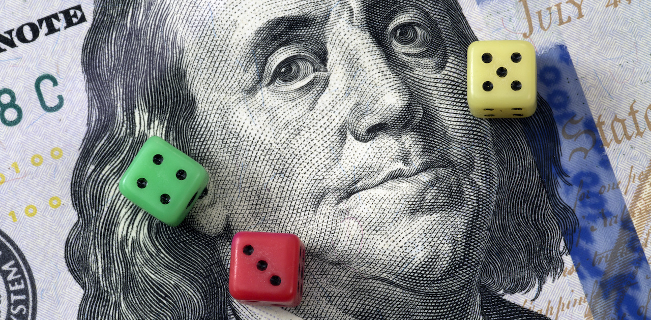 Three colored dice on top of a close up of a $20 bill showing Benjamin Franklin's face.