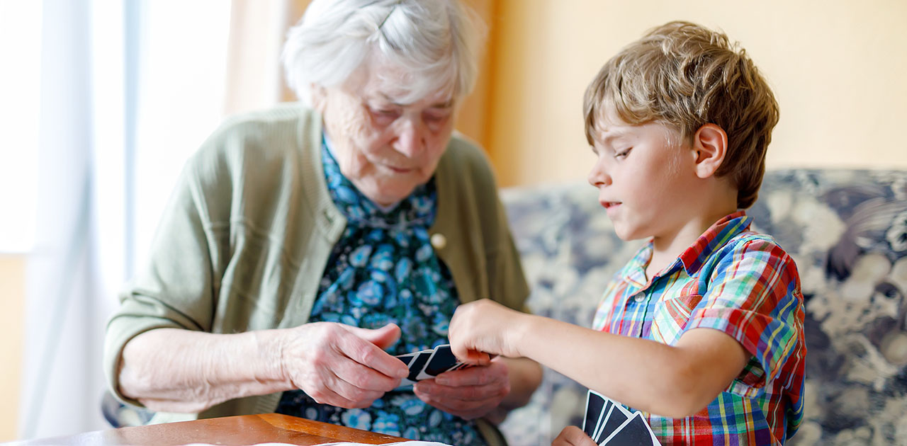 Grandmother and young boy playing a card game together at a table, bonding over a simple family activity.