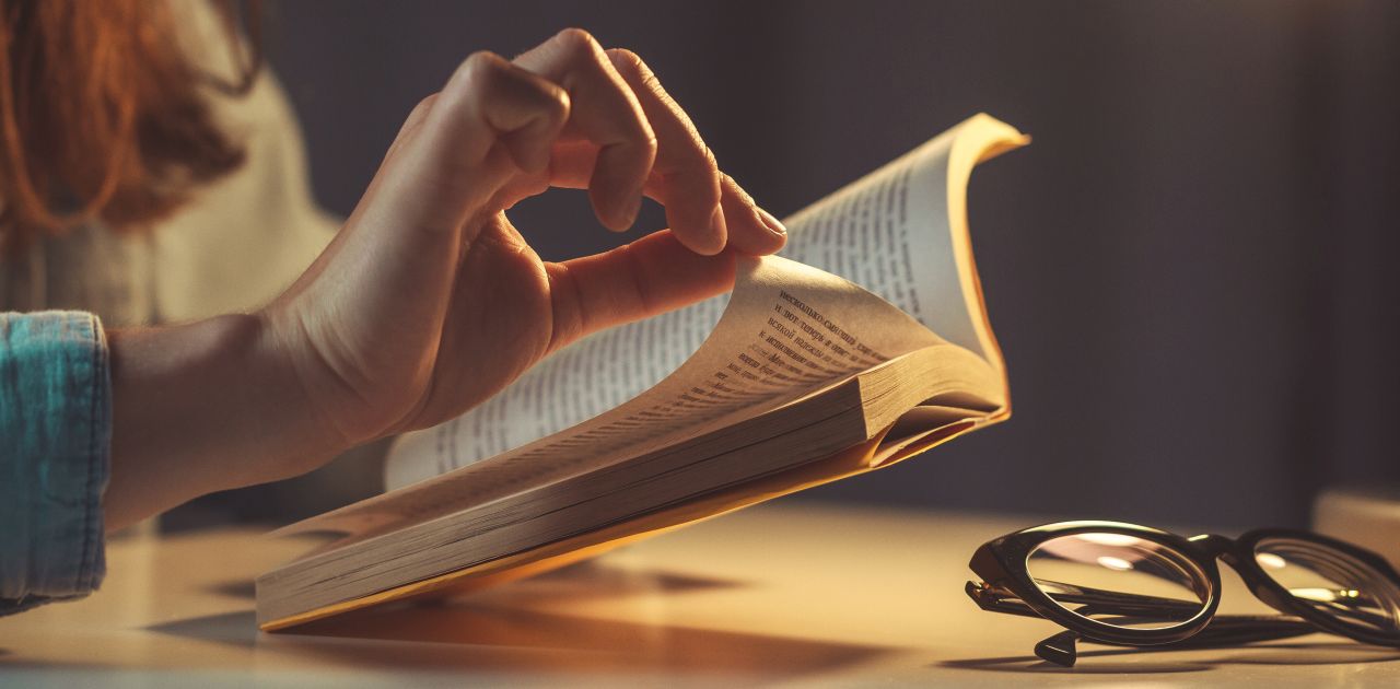 A woman reading a book while turning a page with her hand.